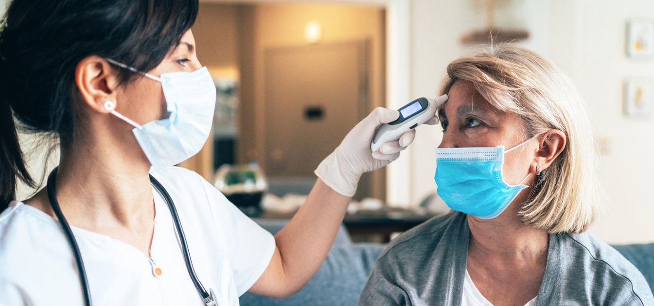 masked nurse takes masked patient's temperature
