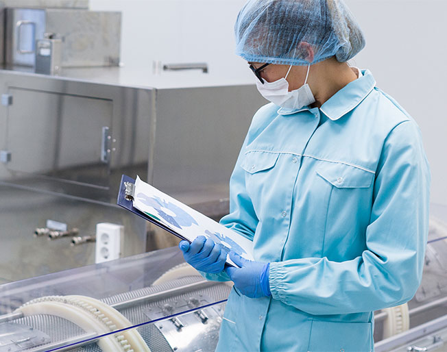 masked researcher holds pad and examines large device