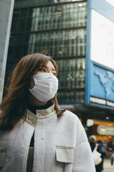 Asian woman wearing face mask walks in city.