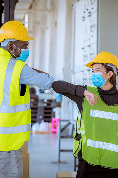 two masked workers in helmets bump elbows