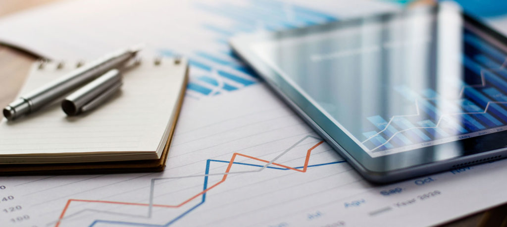 tablet, notepad, and data charts spread across desk