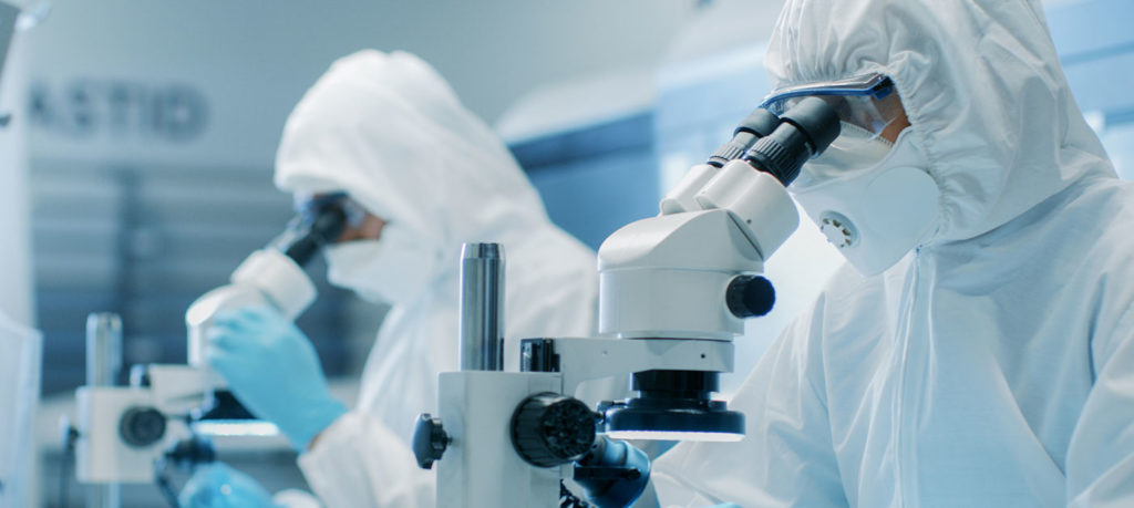 two chemists in full protective gear look into microscopes