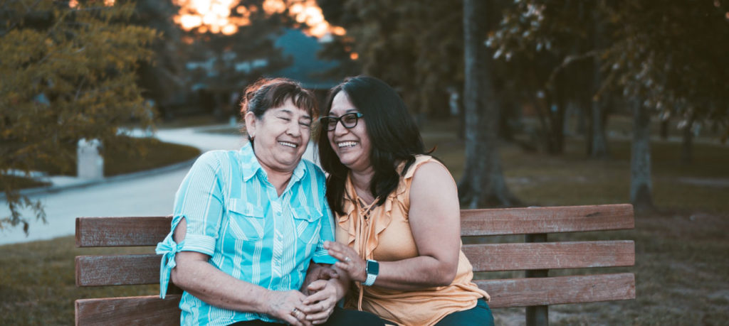 Two senior women laughing together on a park bench