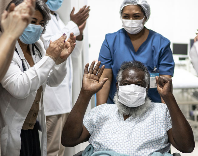 healthcare workers applaud as patient is discharged from hospital in wheelchair