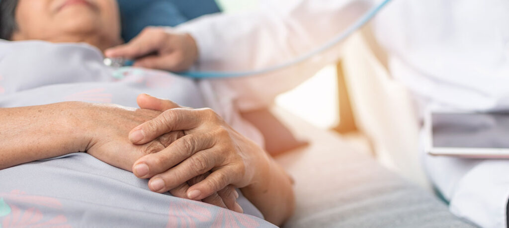 a patient reclines in a hospital bed while someone holds a stethoscope to their chest