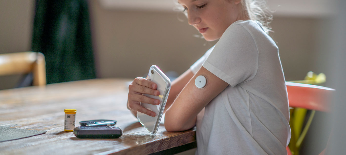 child with diabetes monitoring blood glucose levels with device and phone