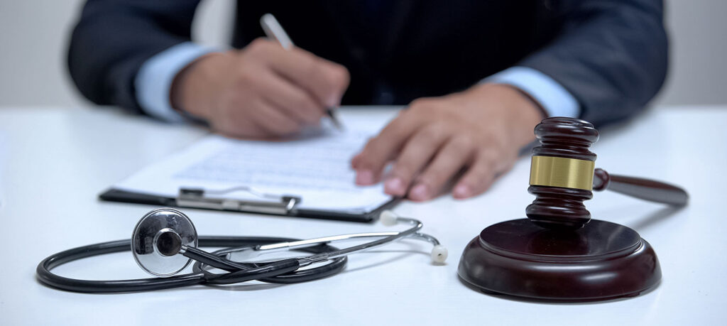 someone signing a document next to a gavel and stethoscope