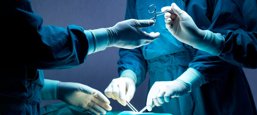 nurse handing scissors to a surgeon while another medical practitioner is also operating on a patient