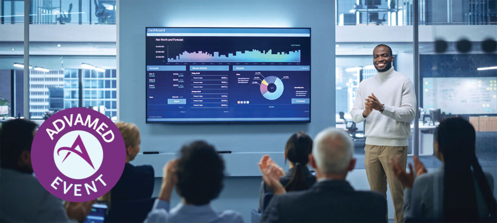 Man standing at the end of his presentation in front of a tv as the audience claps for him