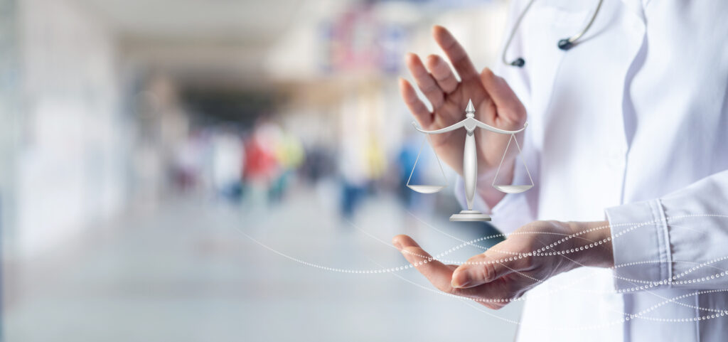 Doctor shows scales of justice on blurred hospital background.