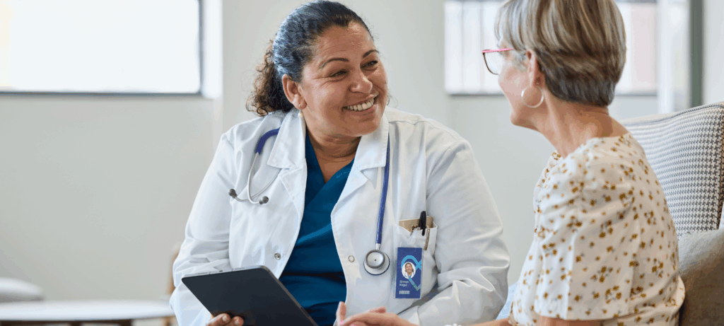 Smiling female physician sharing good news with senior woman at hospital. Doctor is consulting elderly patient.