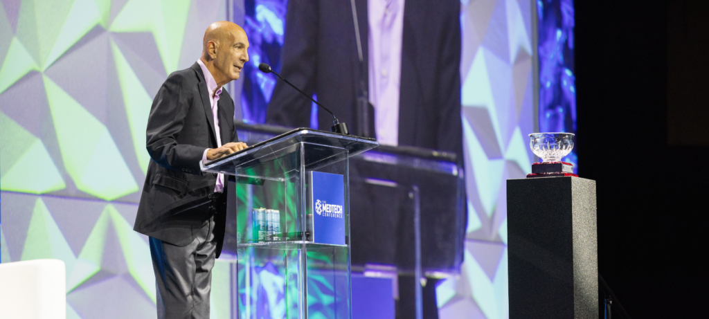 Man in suit on a stage speaking at a podium accepting a an award